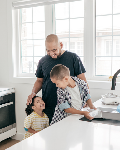Dad stands smiling with his two children in their kitchen.