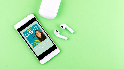 green background with earbuds and case. Laying along side a smartphone that has the Manifesting Clarity Podcast on it. 