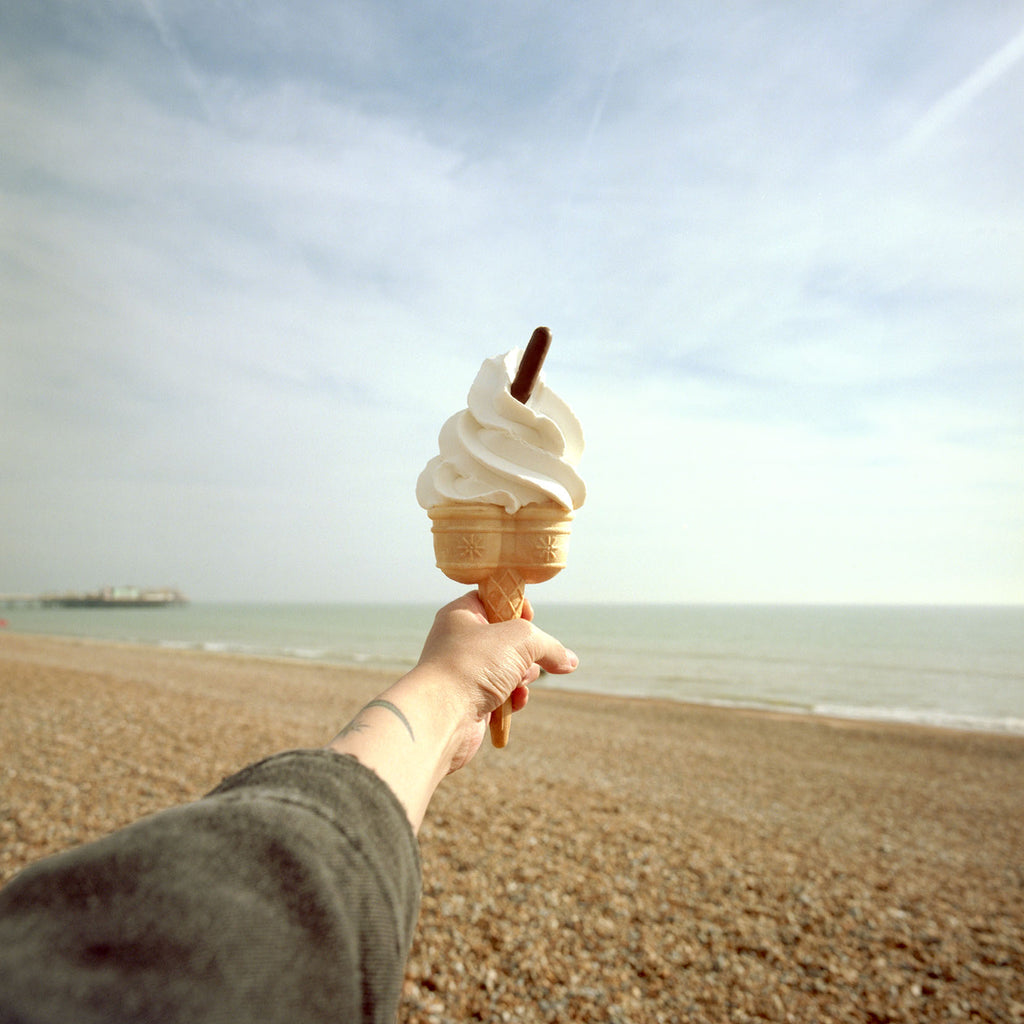 holding an ice cream in a cone with a chocolate flake in the top on the beach.