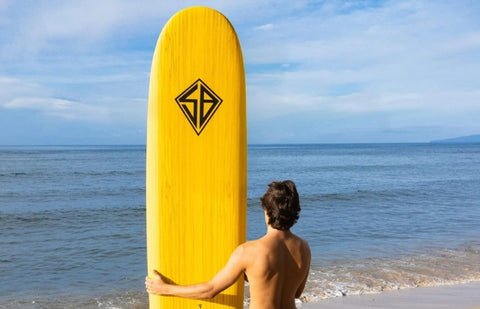 a beginner surfer holding a foam longboard