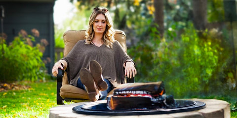 Woman relaxing with their feet up around the Walden Backyards Legacy Series Fire Pit Insert.