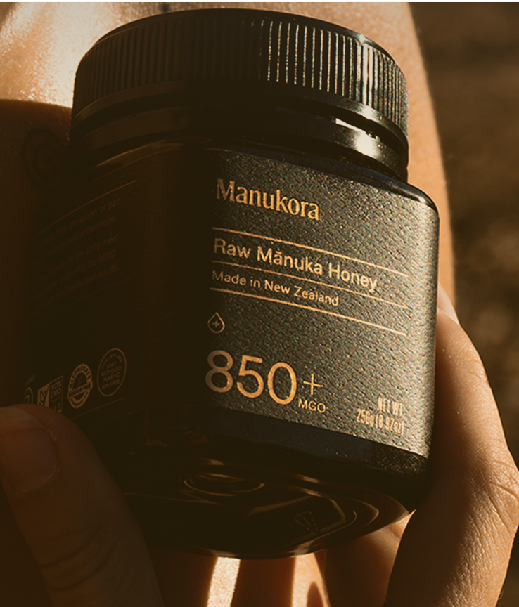 Jar of Manuka honey labeled 'Manukora' held in hand.