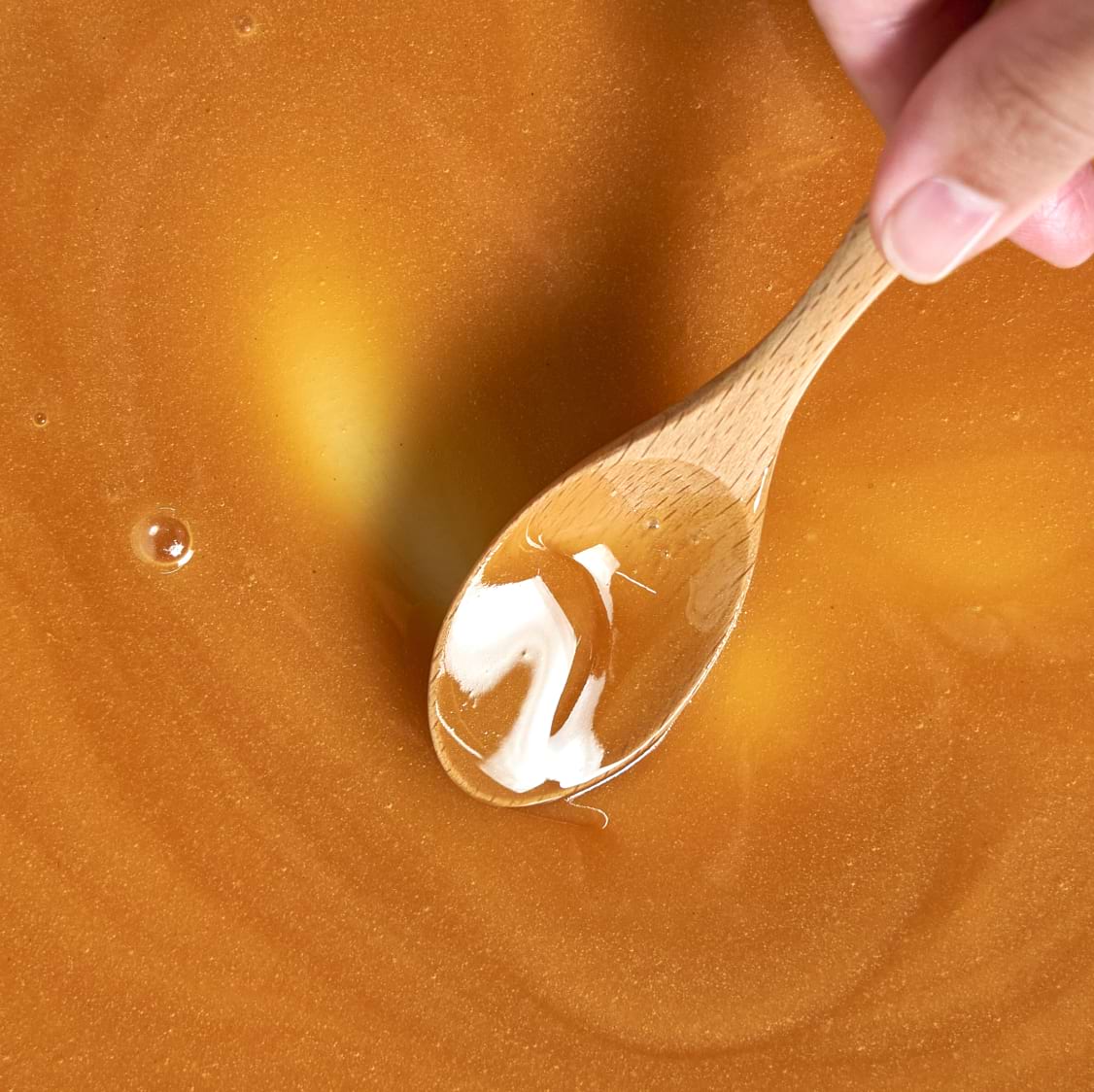 Wooden spoon stirring golden brown liquid, likely caramel or toffee.