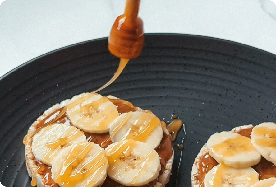 Rice cakes with peanut butter, banana slices, and honey drizzle on a black plate.