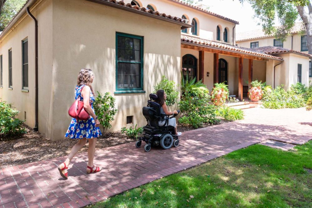 Sylvia Colt-Lacayo and her mother, Amy Colt, visit Stanford University on June 24, 2019. They are outdoors on a brick footpath. Image for article on access to college for disabled students.