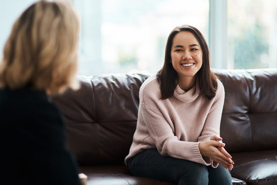 An Autistic person is sitting on a sofa in an office talking to their manager disclosing autism.