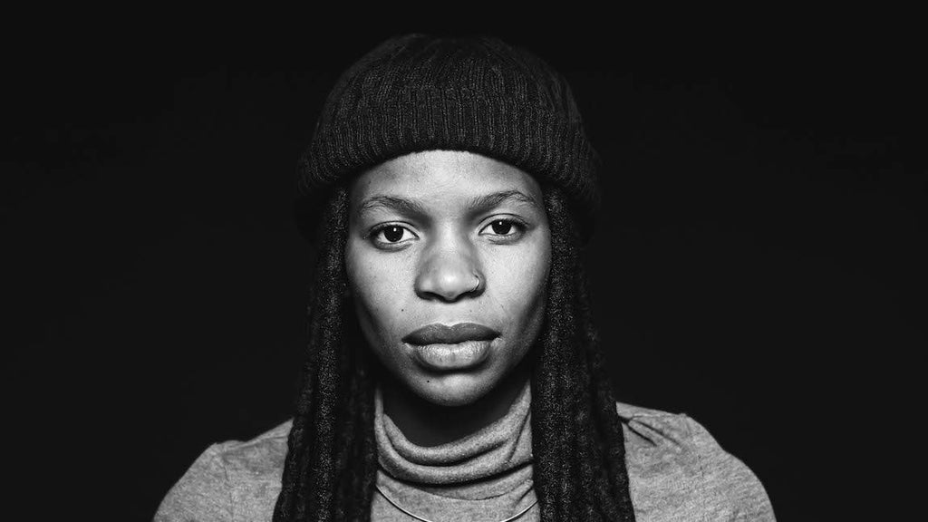 Image for an article on racism and depression. A striking black and white white of an african-american woman with dreadlocks. She has a serious expression on her face and is staring at the camera. Image for an article on 
