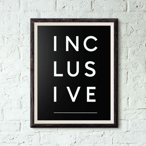 Photo of a framed black inclusive poster on a brick wall. The word inclusive is printed in white over 3 lines, with 3 letters on each line: INC LUS IVE.