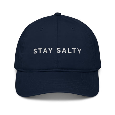 A photo of a navy Stay Salty cap lying flat against a plain background. On the front panel of the cap, the phrase, 'Stay Salty,' is embroidered in white upper case letters.