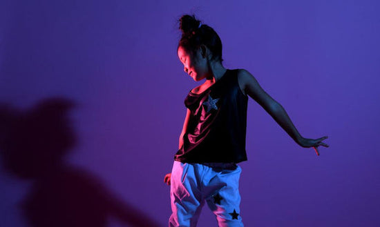 A photo of one pre-teen child participating in dance movement therapy with children. They dancing to pop music and are photographed against a purple background.