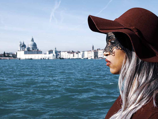 Toma de perfil lateral de un joven que mira hacia adelante y tiene depresión durante sus vacaciones en Venecia.  Ocupan la mayor parte de la derecha de la foto.  Venecia está al fondo. 