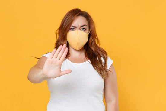 fat shaming doesn't work: a displeased young plus size body positive female is wearing a yellow dress and has a face mask on. She is showing a stop gesture with the palm of her hand towards the camera as if to say, 'stop .. fat shaming doesn't work.'