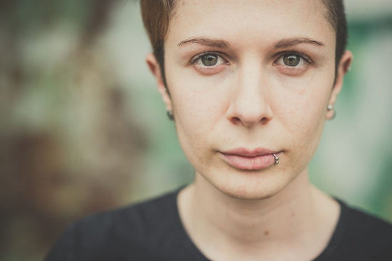 Young stylish disabled and butch person with a lip ring and short hair. They have a serious facial expression.