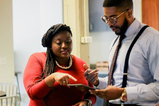 A photo showing how can managers support employees' mental health: a manager wearing a red jumper on the left of the photo is giving guidance to a taller employee on the right of the photo. They are both wearing formal business clothing.