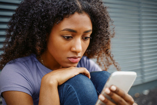 A woman with body image dissatisfaction is looking their phone with a worried depressed expresion.