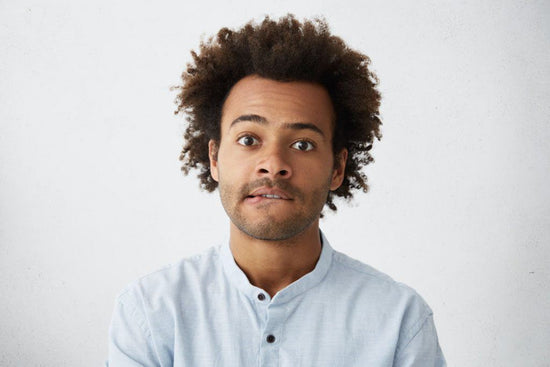 how to talk to a disabled person: a photo of a man with curly hair looking at the camera while biting their bottom lip.