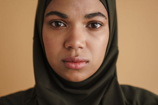 A Black woman in a hijab posing and looking at camera isolated over beige background.