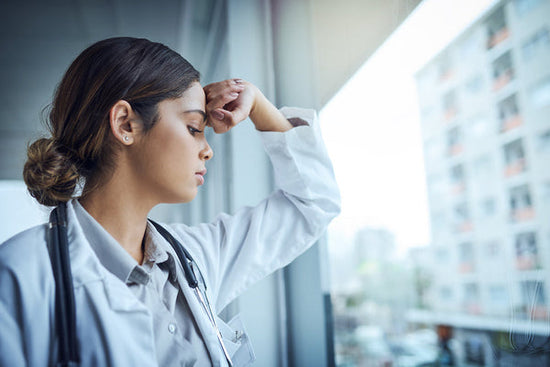 Medicine is not perfect: a young doctor is exhausted, leaning against a window, showing the pressure of perfectionism on doctors.