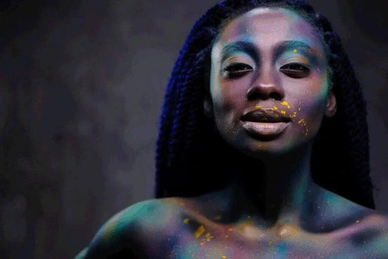 Photo for article on myths about sex addiction. Young woman covered in colored splashes of powder stands assertively in front of dark background.