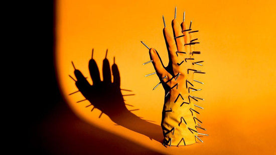 Photograph of the right hand of a pair of rubber gloves for article on Pain and the power of words. The orange and yellow glove is standing upright, fingers into the air, on an orange background. 