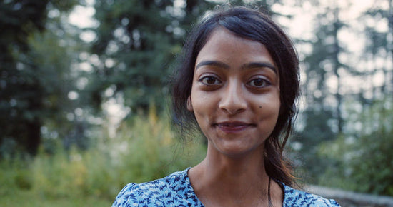 A color photo of a South Asian person standing in a forest for an article about reclaiming sex drive after chronic illness. They are smiling at the camera.