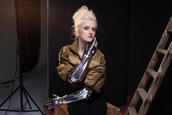 Photo of Tilly Lockey, bionic arm girl, on the set of a photoshoot. Her body faces forward as she looks at the camera. She is wearing an army green oversized bomber jacket and black trousers.