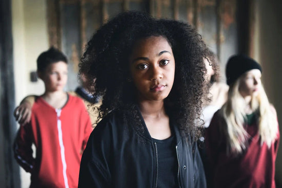 When friends dismiss your illness: a photo of a young woman looking at the camera. Her friends are behind her, blurred, and distant.