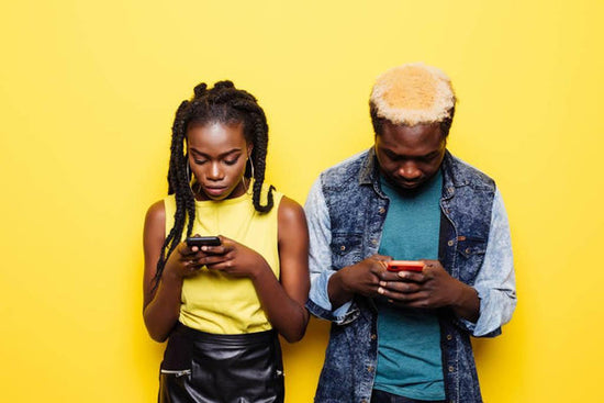 A couple stand next to each other, backs against the wall, looking at their cell phones, avoiding sex, avoiding intimacy.