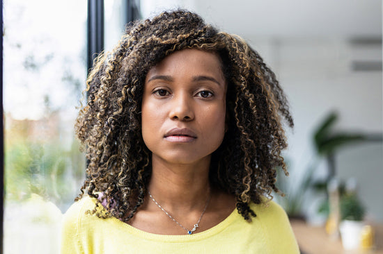 Portrait of a young woman asking, 'Why do I hide physical pain?' as she gazes confidently into the camera, surrounded by the warmth of her home's natural light.