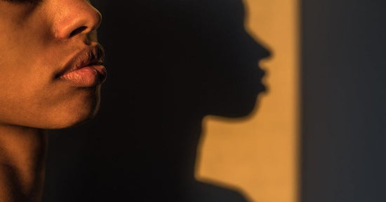 A photo of a person's face, with only the nose, lips and chin visible. Their face casts a shadow a wall. The photo is show at sunset with yellow hues. Photo for an article 