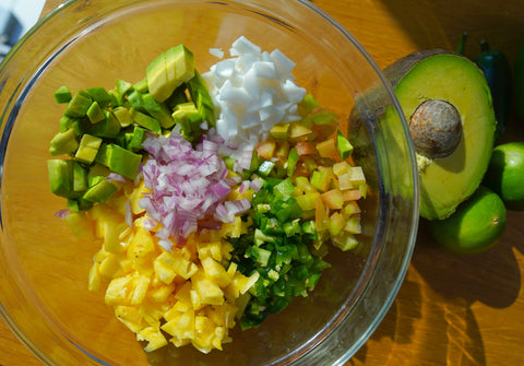 Large glass bowl filled with Copra's organic young Thai coconut meat, diced pineapple, green tomatoes, jalapeños, red onions, avocado, coriander, green bell pepper or green capsicum, salt, pepper, lime juice and olive oil