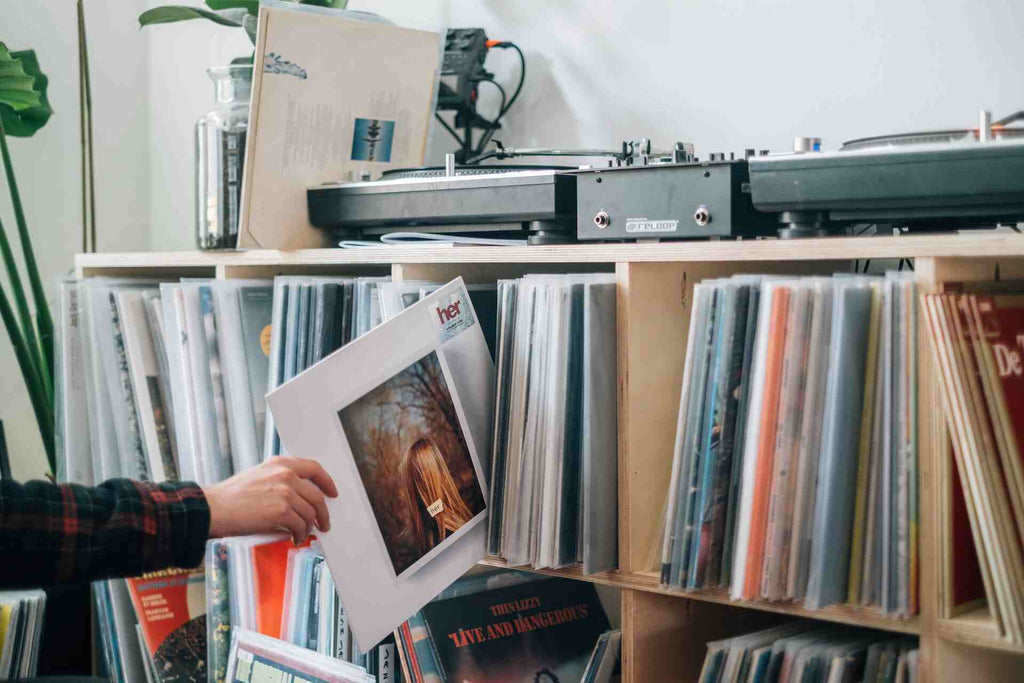 a person holds a record in between a stack of records in a shelf