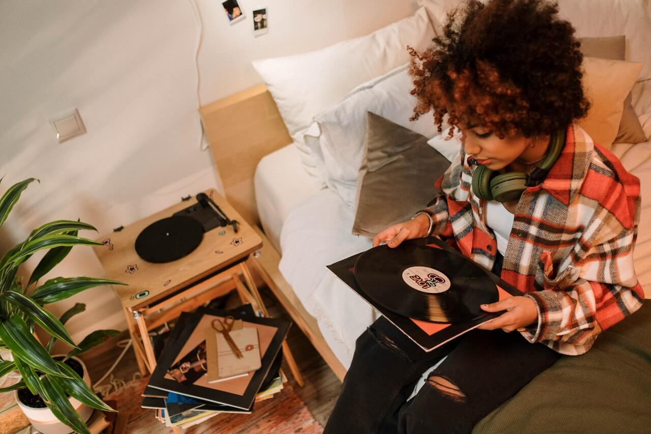 Person in plaid shirt sits on edge of bed looking at vinyl record