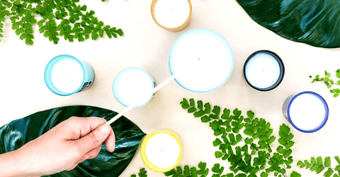 A person lighting a scented candle with a few other candles next to it.