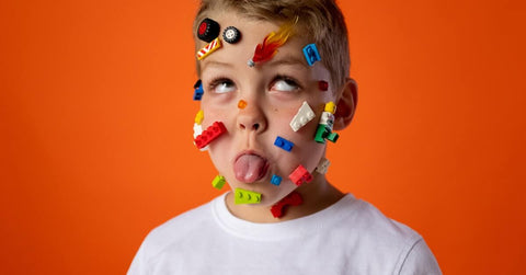 A boy making a silly face with legos all over his face.