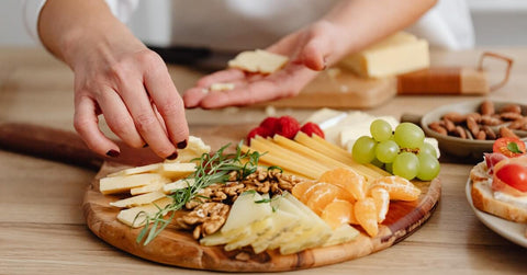 A person putting food on a charcuterie board, which is one of the best gift ideas for the person who loves to entertain. 