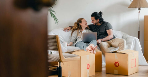 Couple sitting on a couch and looking at a laptop after moving into a new home