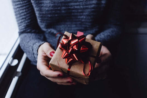 A person holding one of the gifts for organizing enthusiasts in a brown box with a large red bow.