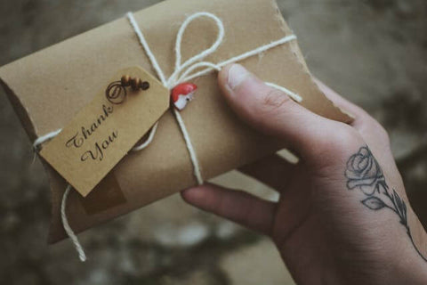 A person holding a small gift with a “Thank You” card