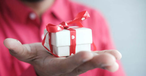 A person giving a small gift in a white box with a red ribbon