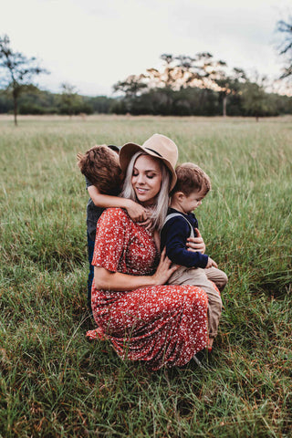 mother in a red maxi dress embracing her two boys