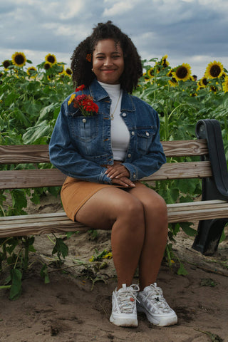Happy girl sitting on a bench and posing in denim jacket and brown mini skirt