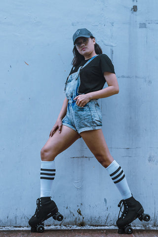 Woman posing with roller skates, denim rompers, and knee socks