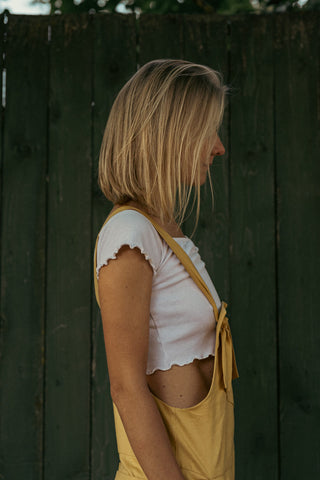 Side photo of a young woman posing in a yellow romper and a white crop top