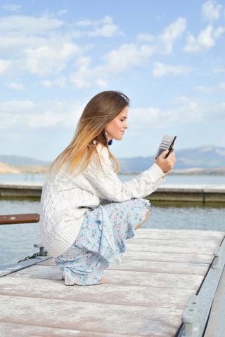 Girl looking at her phone wearing a blue skirt and a knit sweater
