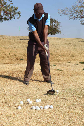 A man playing golf wearing a black sleeveless knit vest over a polo shirt and long trousers