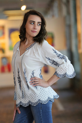 Woman posing with a white tunic with blue embroidery and skinny jeans