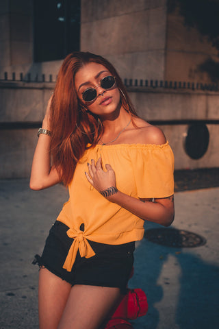 Girl posing with a yellow off-the-shoulder top and black shorts