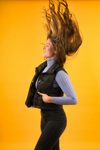 Girl swinging her hair and wearing jeans and a padded vest over a turtleneck 