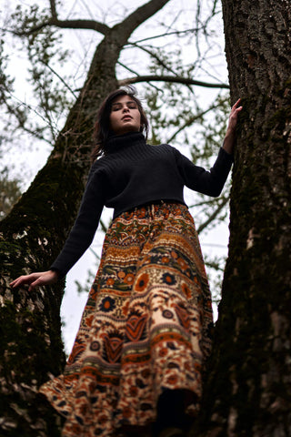 Woman posing under the trees in long brown patterned skirt and a black turtleneck